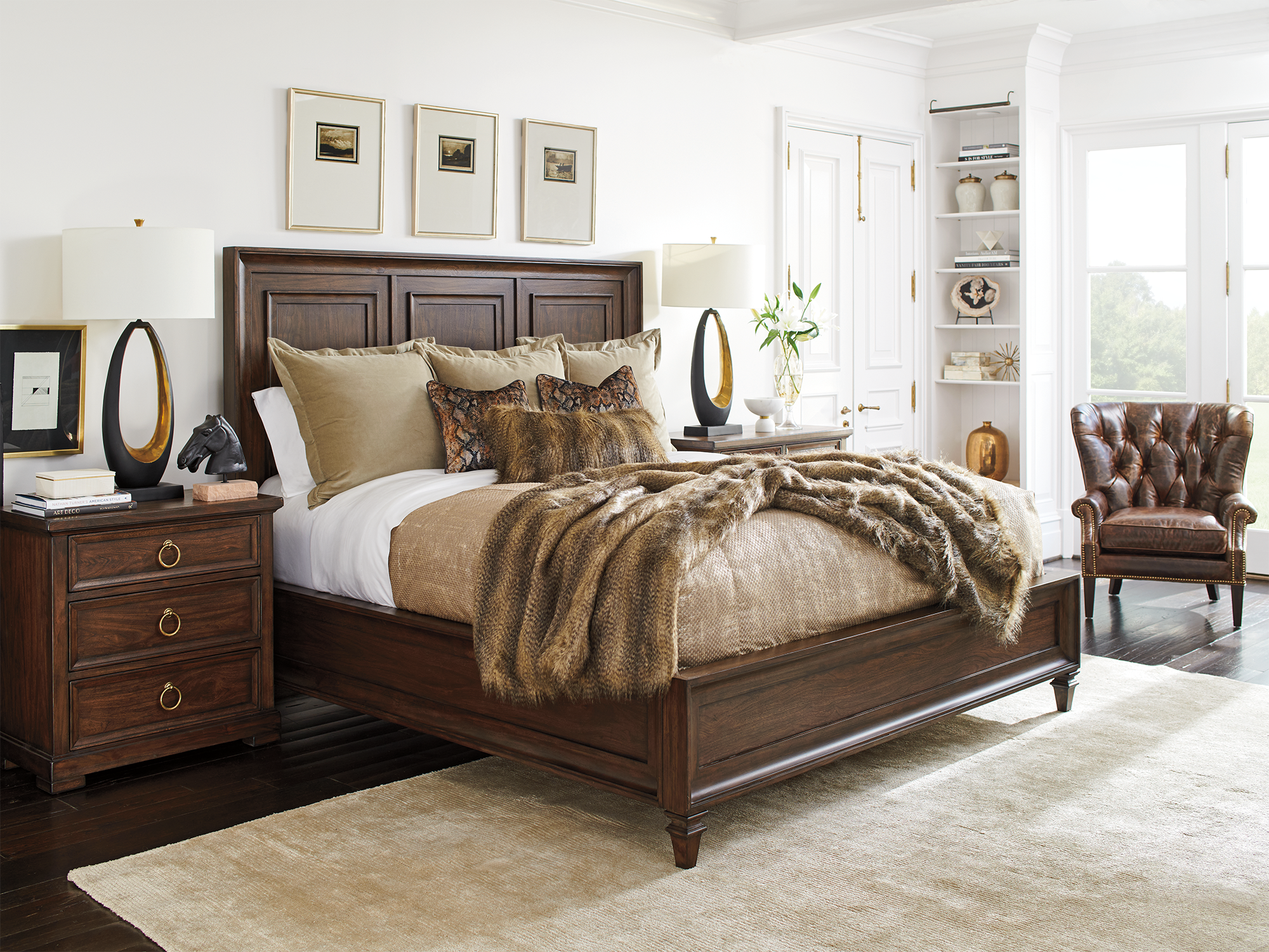 Lexington Silverado — masculine traditional bedroom featuring a dark wood paneled statement bed, a three-drawer nightstand with gold ring pulls, and a tufted leather wing chair accented by faux-fur bedding.