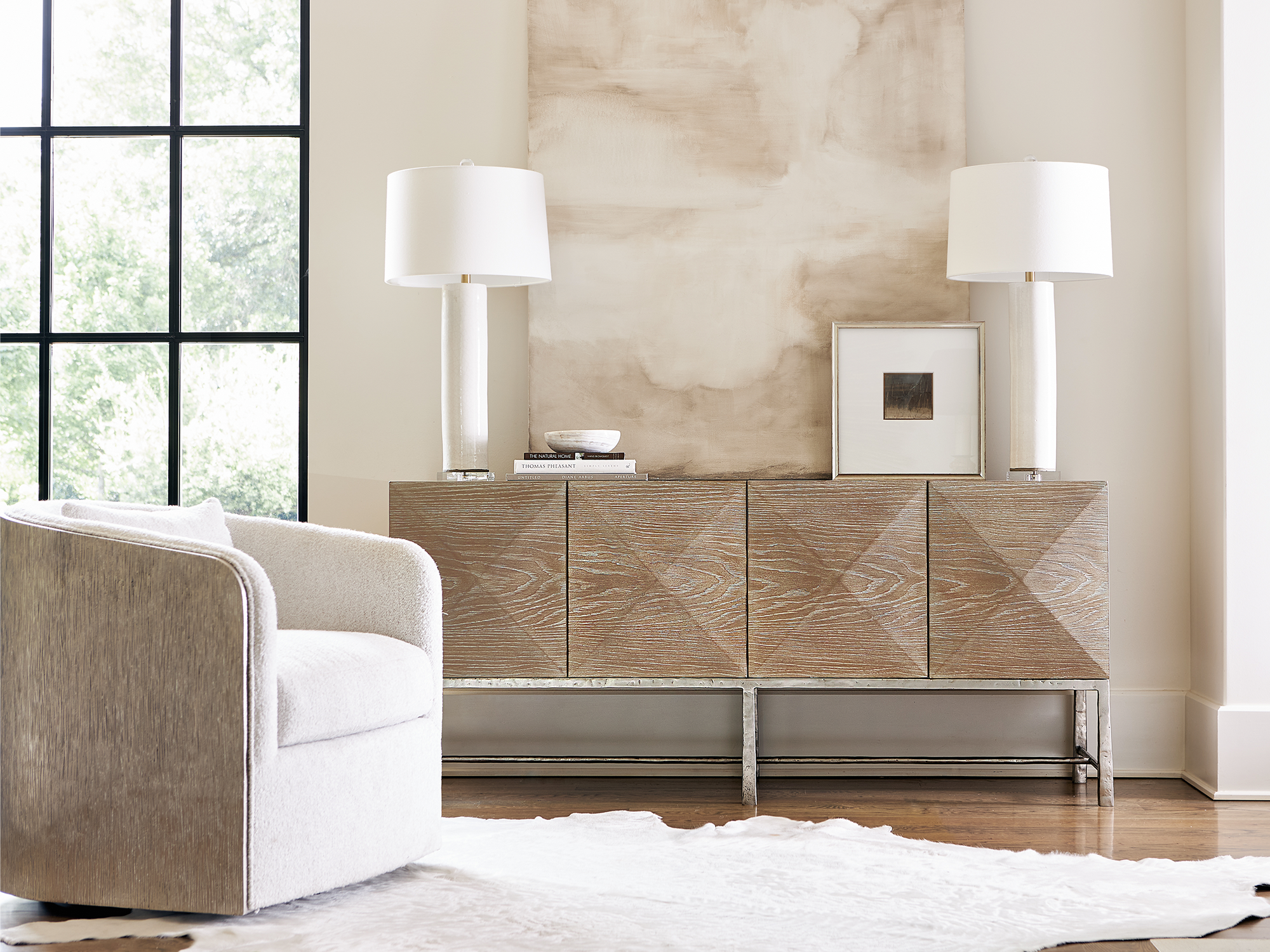 Bernhardt Aventura — modern minimalist entryway featuring a four-door sideboard with a faceted diamond-patterned wood face on a silver metal base, paired with a cream bouclé swivel chair.