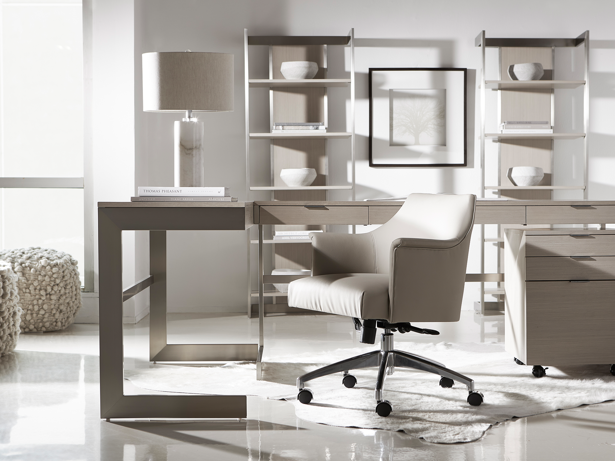 Bernhardt Axiom — ultra-modern home office featuring a light oak desk with a cantilevered metal frame, a leather executive swivel chair, and matching open-shelf etageres with champagne-finish accents.