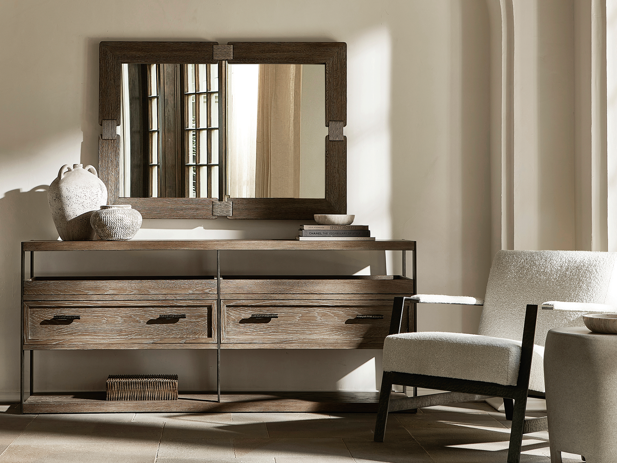 Bernhardt Casa Paros — rustic modern entryway or living space featuring a long wire-brushed oak console with iron accents, a matching framed mirror, and a sleek white bouclé accent chair with dark wood arms in a warm, textured interior.