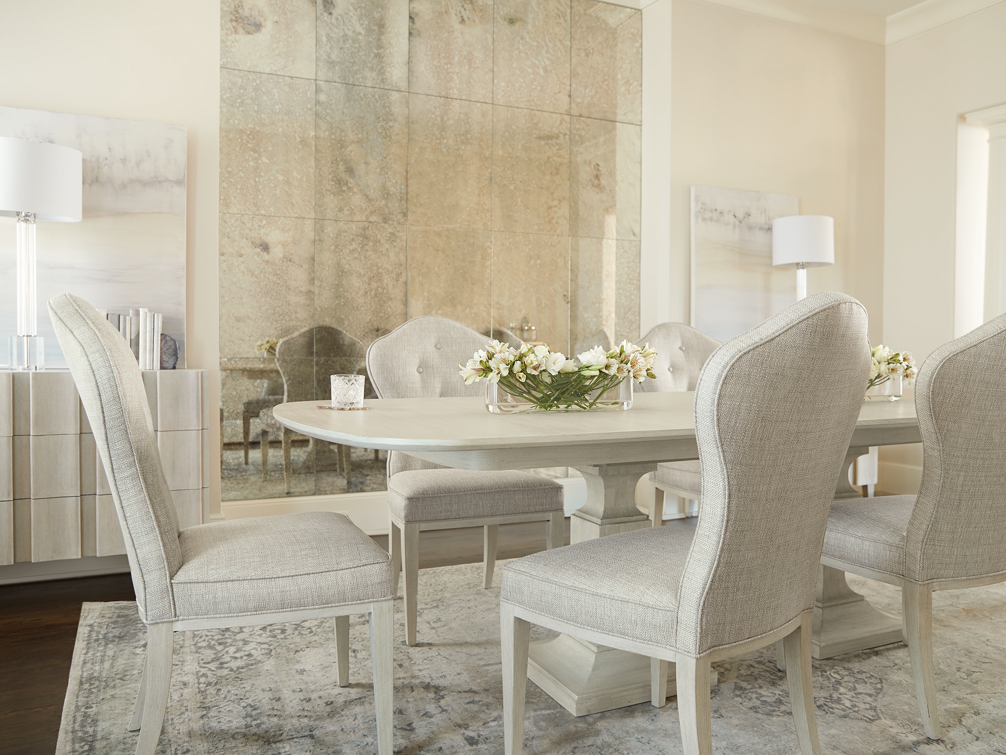 Bernhardt East Hampton — elegant transitional dining room featuring a light-wash wood trestle table, paired with upholstered shield-back dining chairs, set against a stunning antiqued mirror accent wall and a neutral patterned rug.