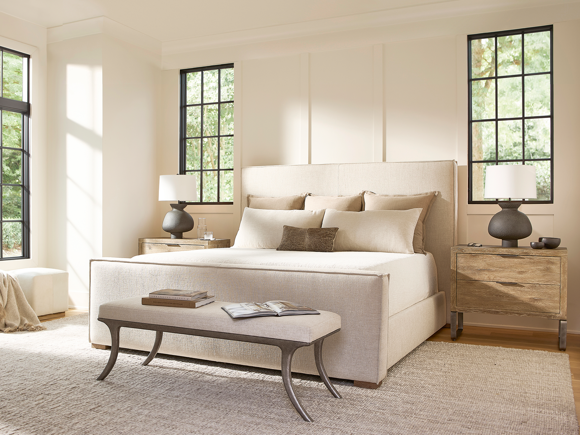 Bernhardt Tribeca — High-profile upholstered shelter bed in neutral linen fabric defines this warm contemporary bedroom. Features rustic oak nightstands with iron legs, a cast-metal bench, and textured gourd-shaped lamps in natural light.