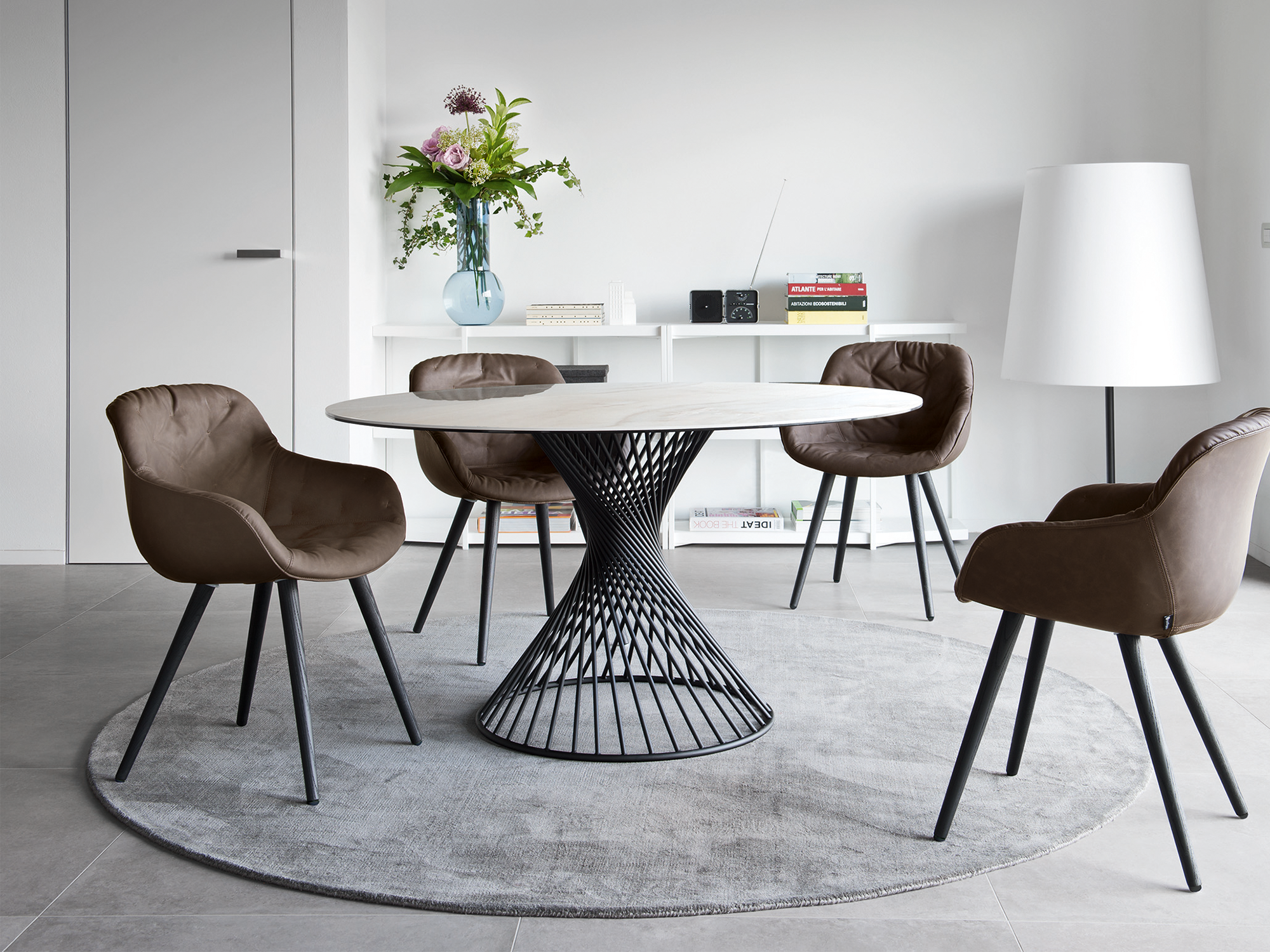Calligaris Vortex — minimalist modern dining room featuring a round marble-top table with a black sculptural wire base and brown tufted leather armchairs set on a circular grey rug.