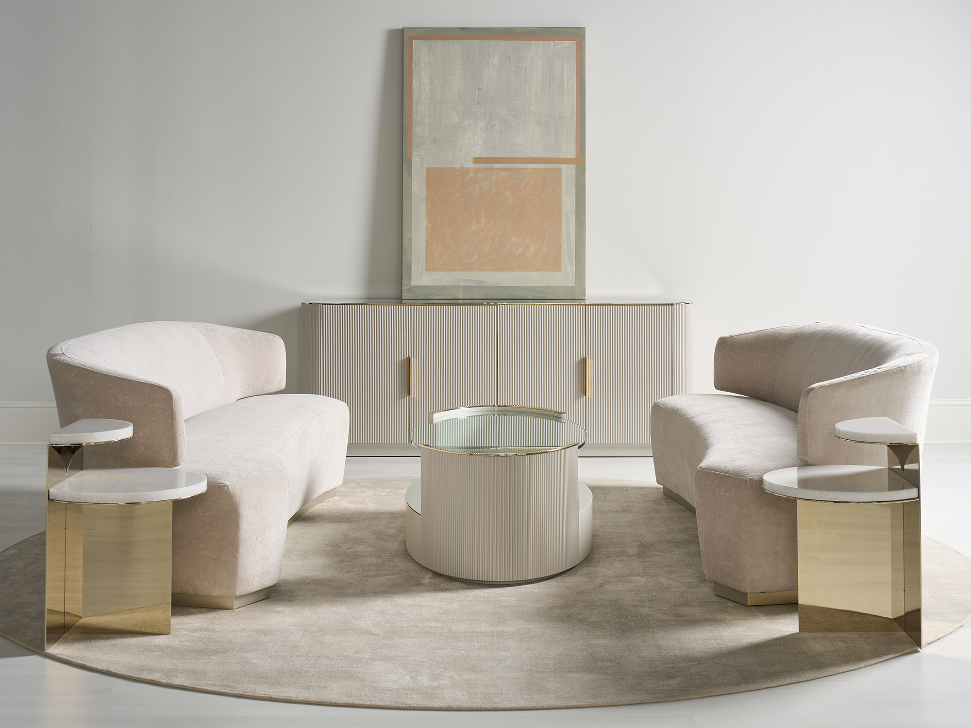 Caracole Classic Collection — elegant living room furniture set featuring curved blush-velvet loveseats with gold-finished bases, a fluted cylindrical coffee table with a glass top, and tiered marble and gold metal end tables.