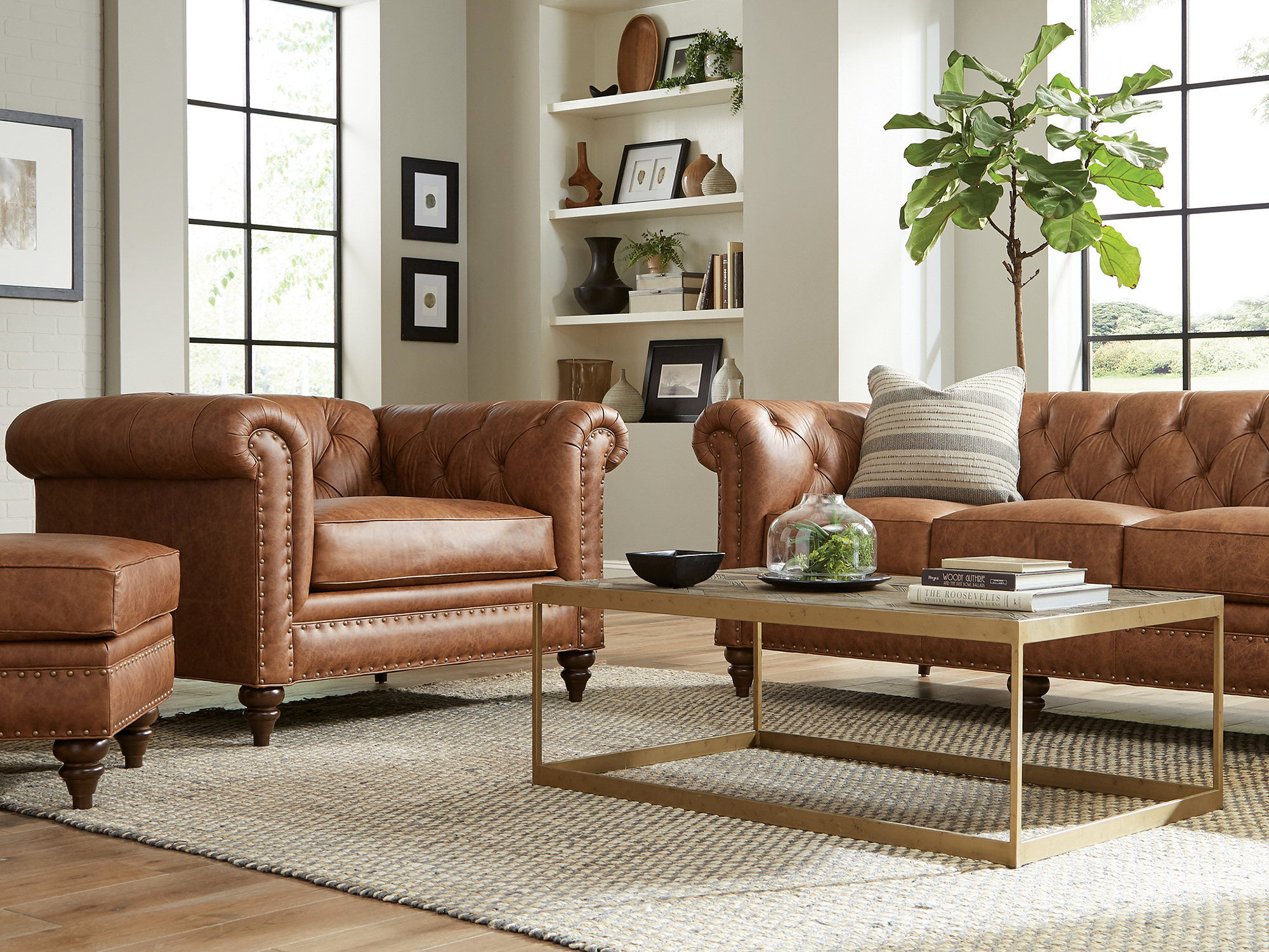 Craftmaster CM Leather — traditional living room set featuring a cognac brown leather Chesterfield sofa and matching armchair with deep button tufting and nailhead trim, paired with a modern gold-framed coffee table.