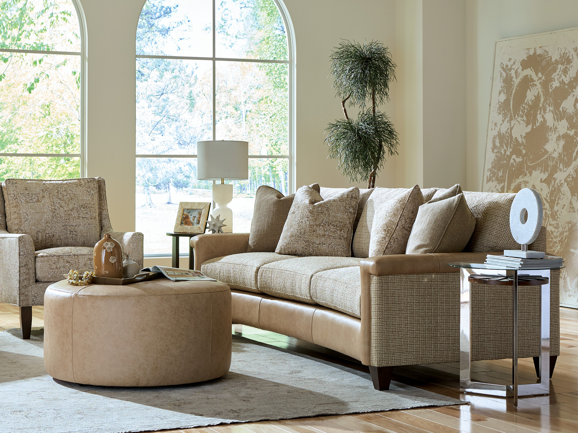 Craftmaster Custom Blends — Mixed-media sofa with tan leather accents and textured upholstery, paired with an oversized round leather ottoman and patterned accent chair. A bright, transitional living room set in an elegant arched-window space.