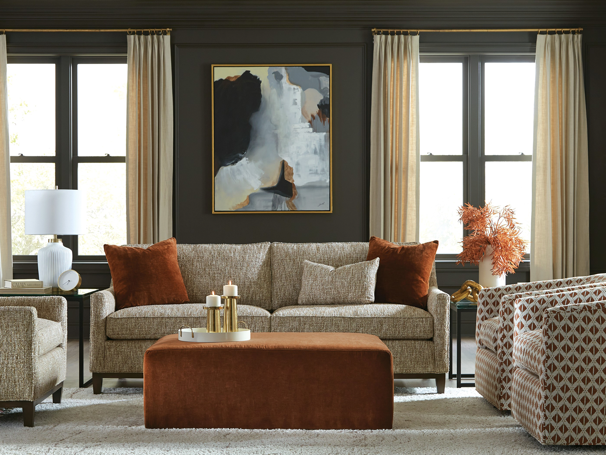 Craftmaster New Traditions — Neutral textured sofa with burnt orange velvet pillows and a matching rust velvet ottoman. This sophisticated transitional living room features geometric swivel chairs against a moody, dark-paneled wall.