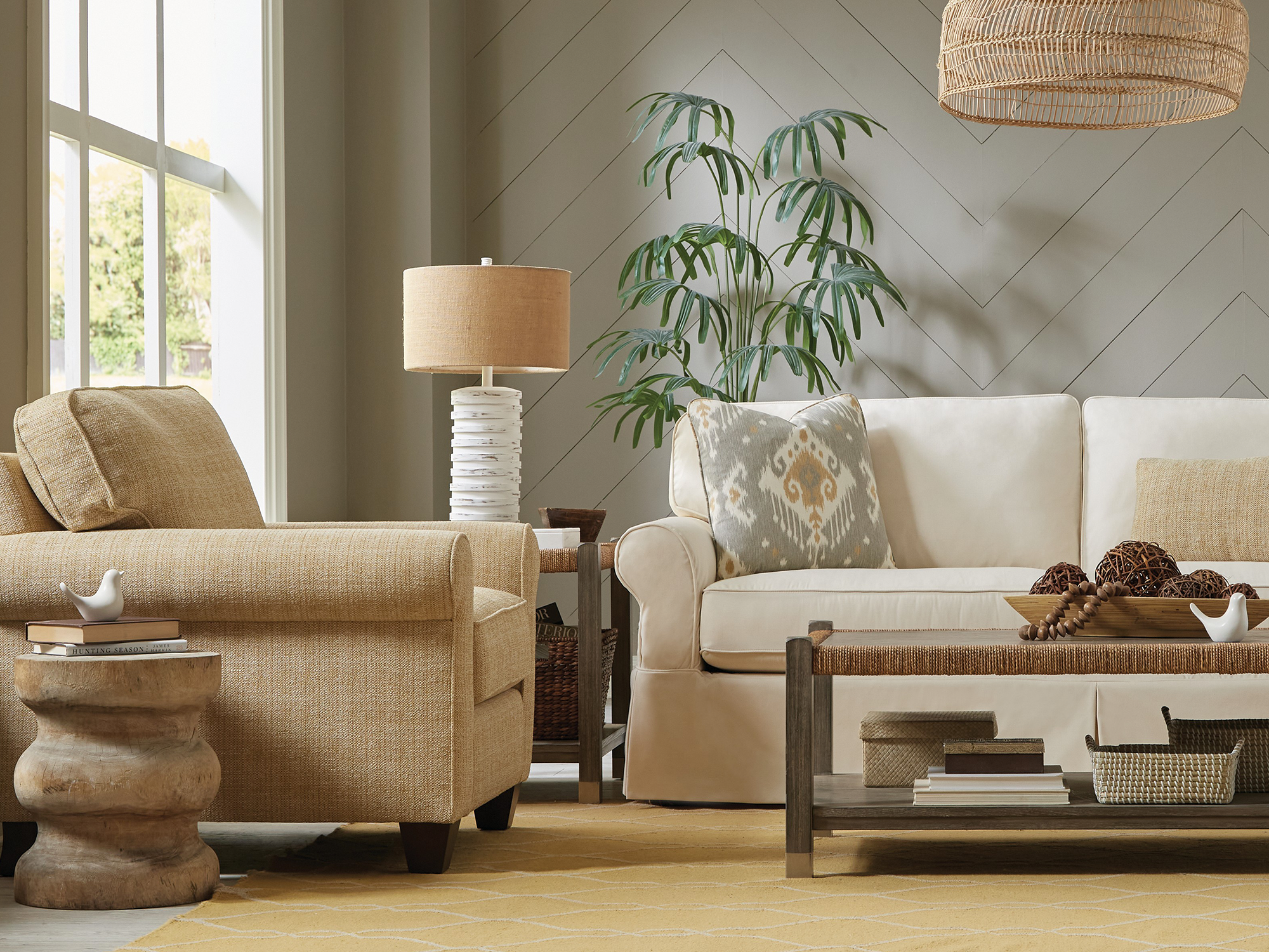 Craftmaster Washable Slipcovers — coastal-inspired living room featuring a cream slipcovered sofa with rolled arms, a textured golden-tan armchair, and a woven wood coffee table set against a gray chevron-patterned accent wall.