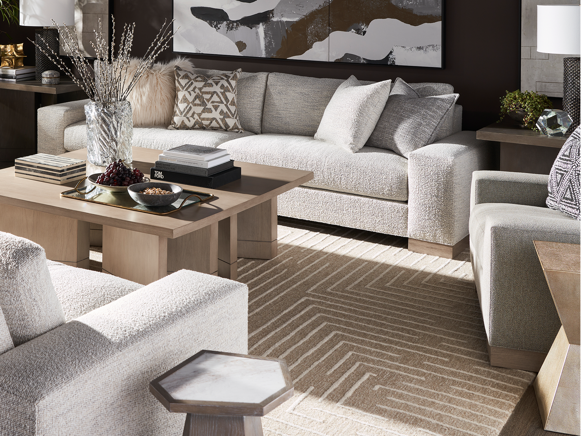 Feizy — contemporary living room featuring a tan and cream geometric patterned area rug, paired with a light grey textured sofa and matching armchairs, a large square oak coffee table, and a hexagonal marble-top side table.