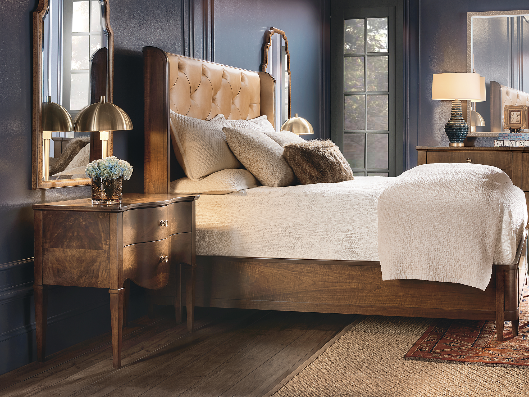 Hooker Furniture — traditional bedroom set featuring a wingback bed with a tan button-tufted leather headboard and a matching walnut-finish nightstand with a decorative scalloped apron and burl wood veneers.
