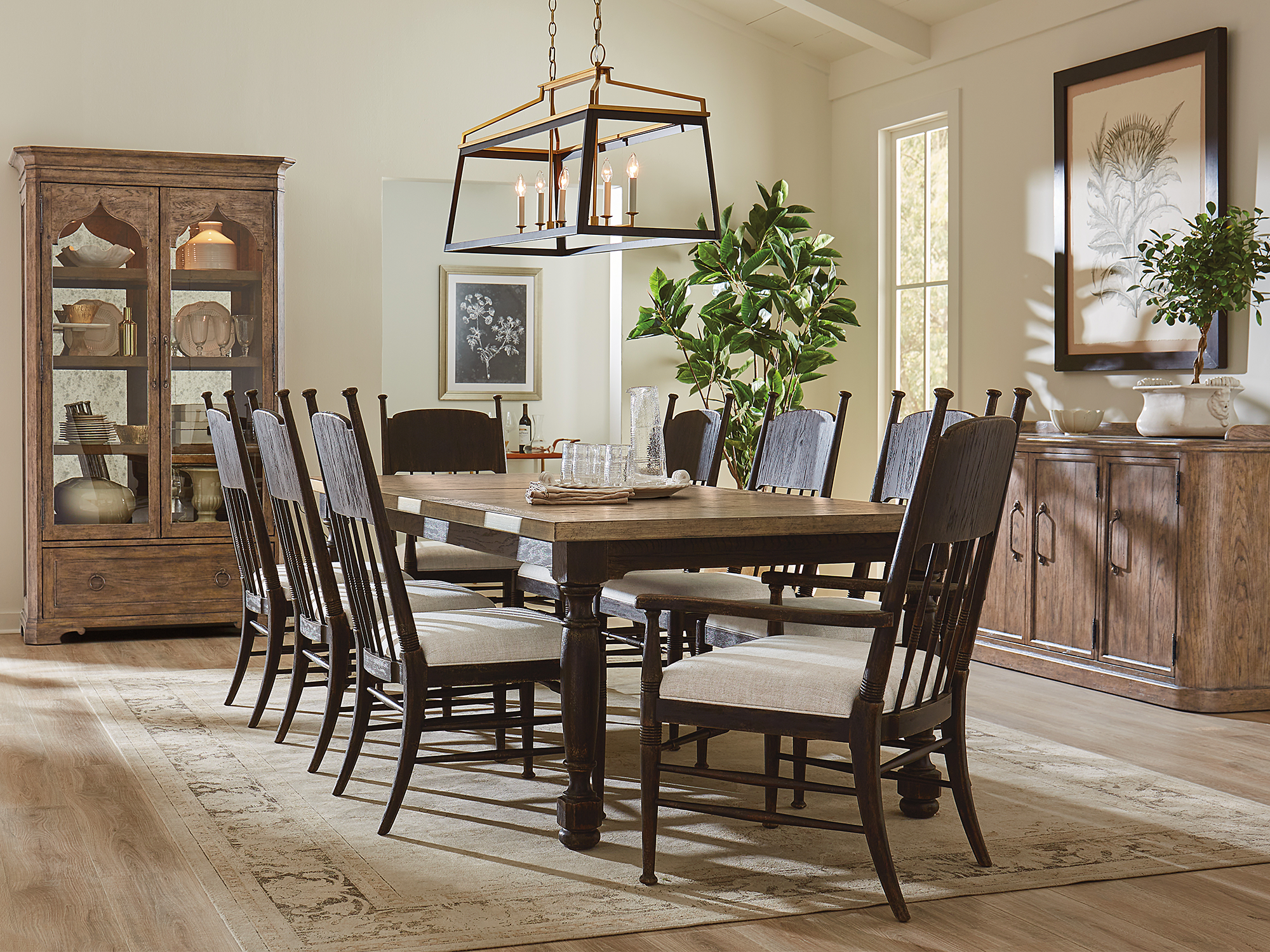Hooker Furniture Americana — classic farmhouse dining room featuring a two-toned rectangular table with turned legs, high-back spindle chairs in a dark finish, and a rustic arched-top china cabinet.