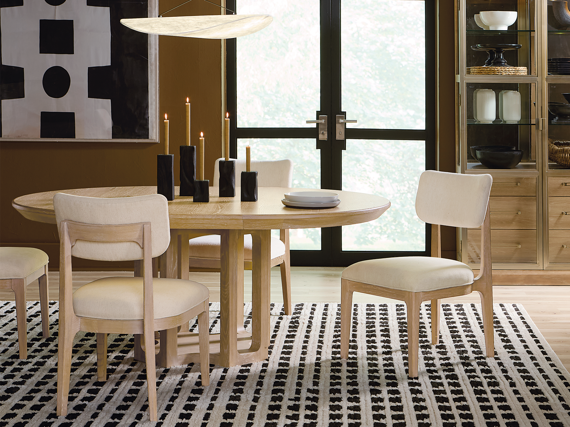 Hooker Furniture — Banyon Bay collection organic modern dining room featuring a light oak round pedestal table and matching upholstered chairs on a geometric black and white rug.