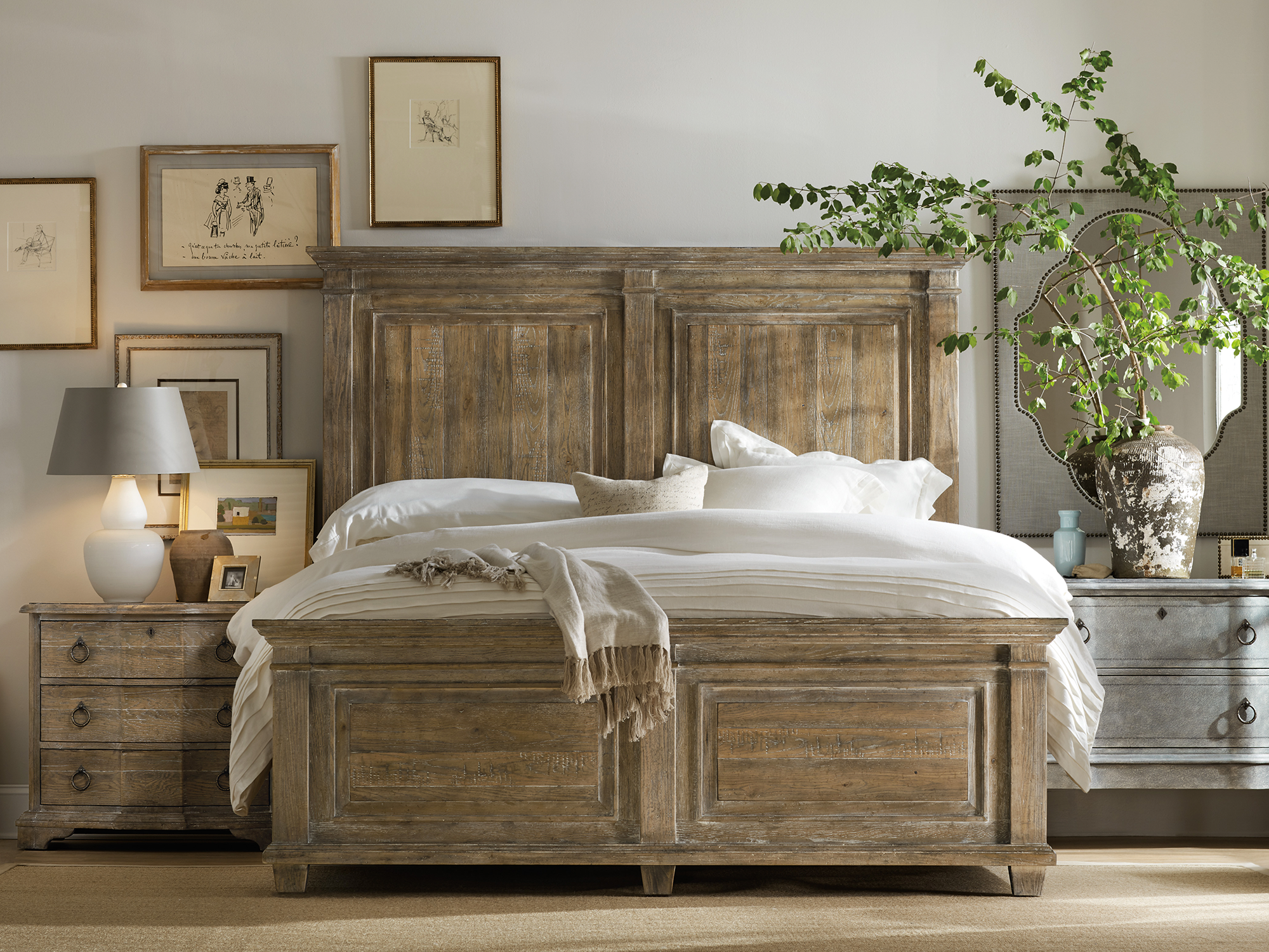 Hooker Furniture Boheme — soulful European-inspired bedroom featuring a massive distressed-wood panel bed, antique-style gray bachelors chest, and a gallery wall of vintage sketches.