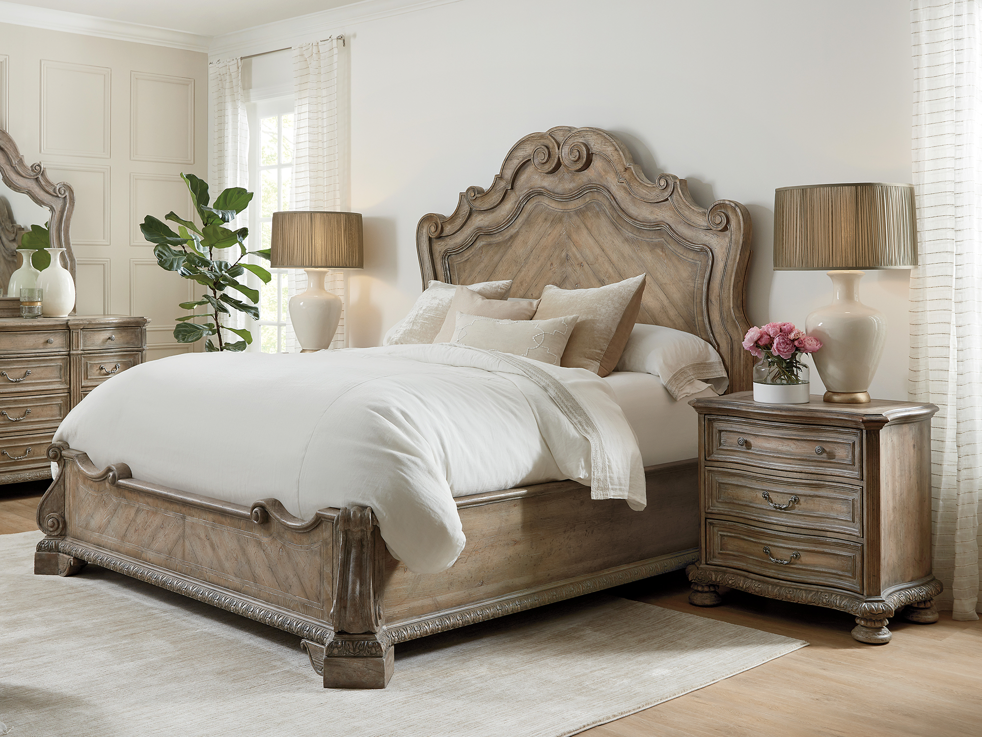Hooker Furniture Castella — grand European traditional bedroom featuring a sprawling mansion bed with a scrolled acanthus-leaf headboard and a matching three-drawer nightstand in a weathered oak finish.