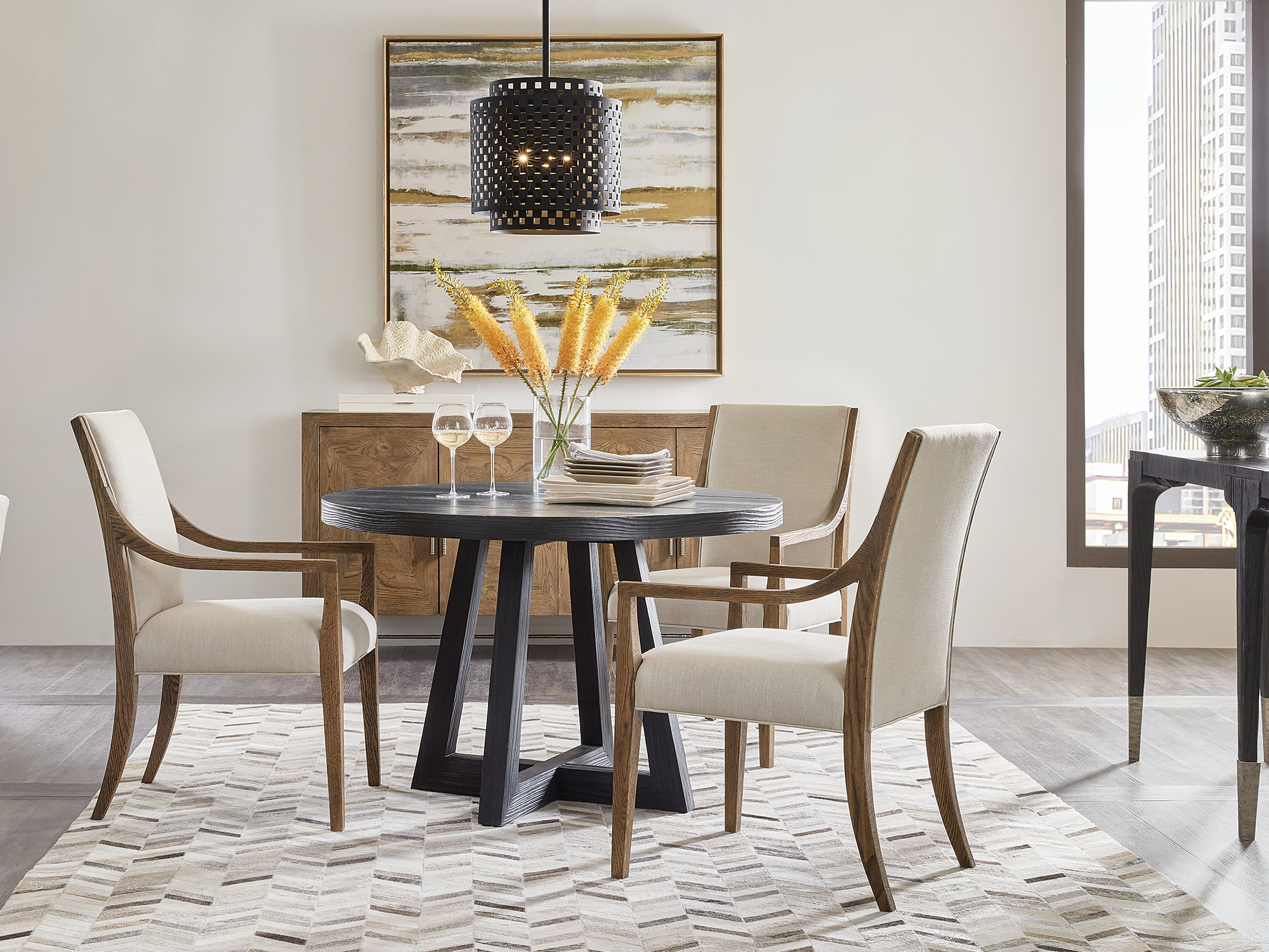 Hooker Furniture Chapman — urban industrial dining room featuring a round black-oak table with a geometric X-base, slope-arm upholstered chairs, and a black perforated metal pendant light.