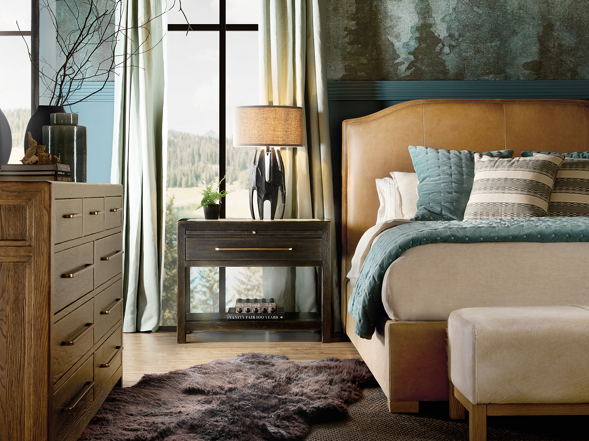 Hooker Furniture Driftwood — moody mountain-modern bedroom featuring a camel leather camelback bed, dark-charcoal nightstand, and oak dresser against a scenic alpine window view.