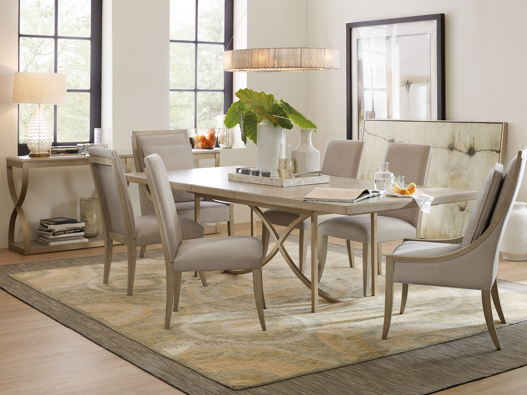 Hooker Furniture Elixir — glam transitional dining room featuring a light walnut rectangular table with a champagne gold metal trestle base, paired with slope-arm upholstered chairs.