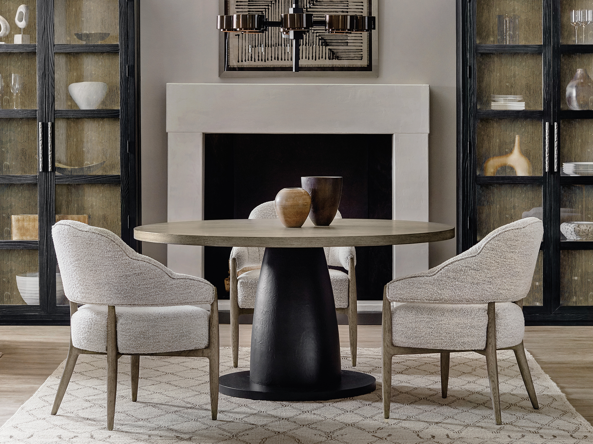 Hooker Furniture Linville Falls — soft-modern dining room featuring a light-oak trestle table with organic live-edge details, charcoal slope-arm chairs, and a grand arched black-iron china cabinet.