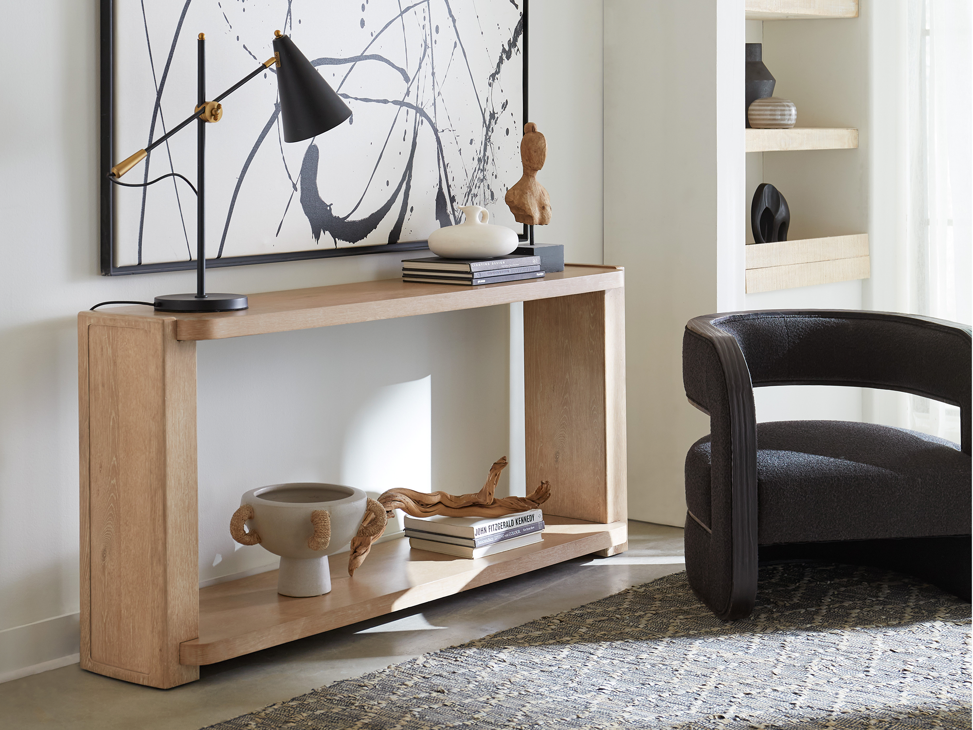 Hooker Furniture Retreat — minimalist organic hallway vignette featuring a light-oak waterfall console table with rounded edges, a black barrel-back accent chair, and mid-century modern lighting.