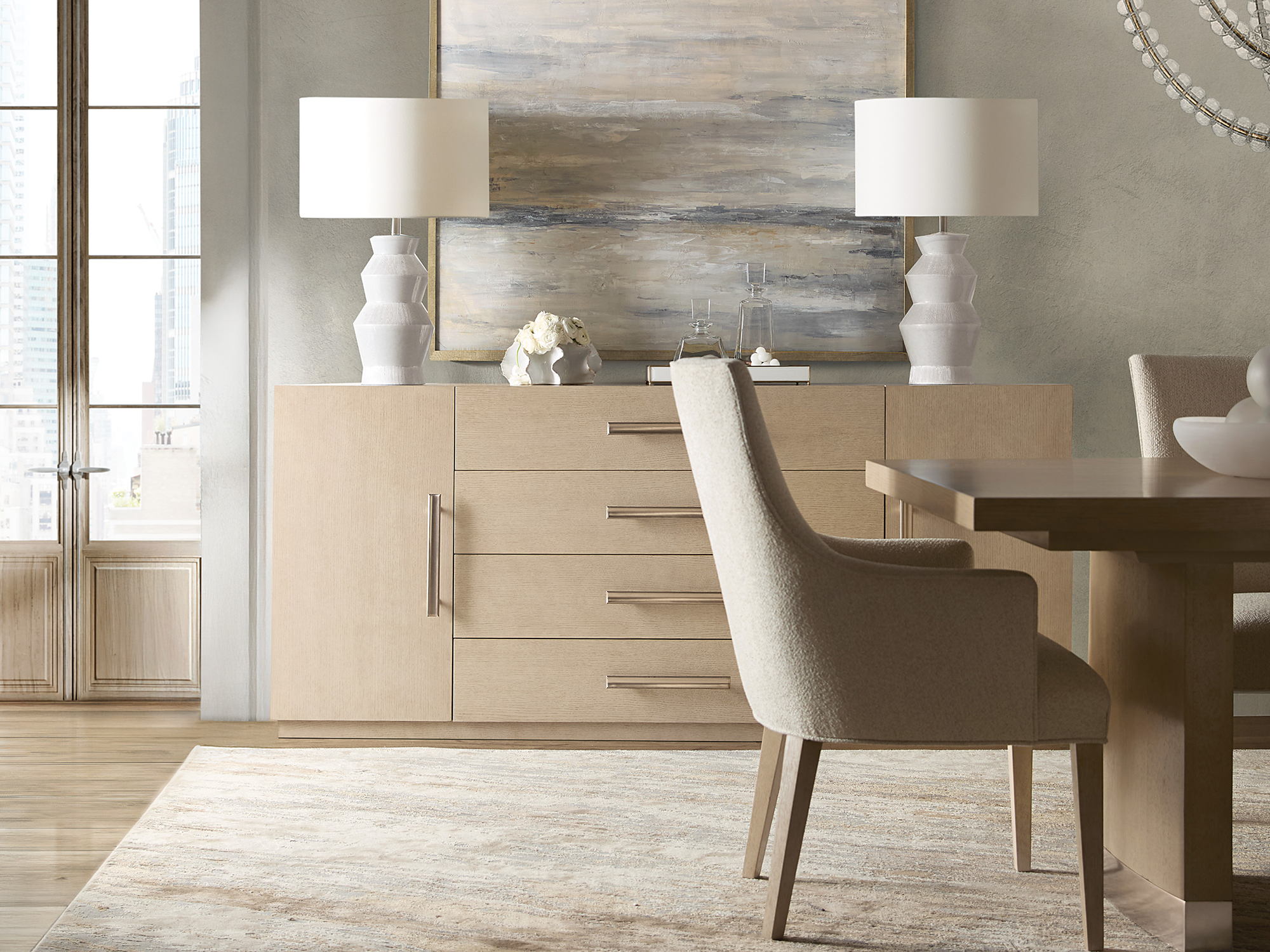 Hooker Furniture — Westwood collection modern dining room featuring a light oak buffet with sleek metal hardware, a matching pedestal dining table, and cream upholstered armchairs.