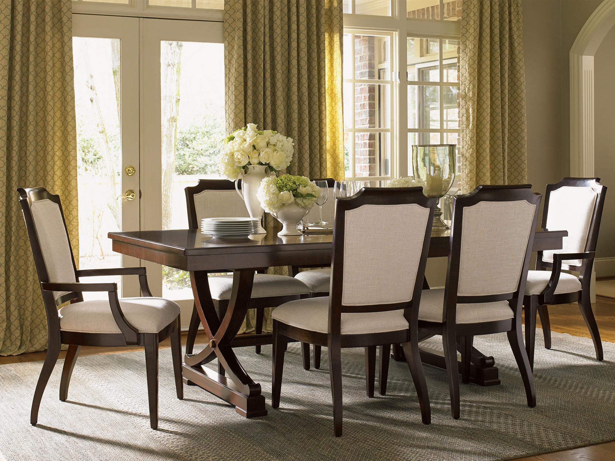 Lexington Kensington Place — X-base trestle dining table in a rich cherry finish paired with upholstered shield-back chairs. This traditional dining space features elegant patterned drapery and a neutral textured rug for a sophisticated, timeless look.