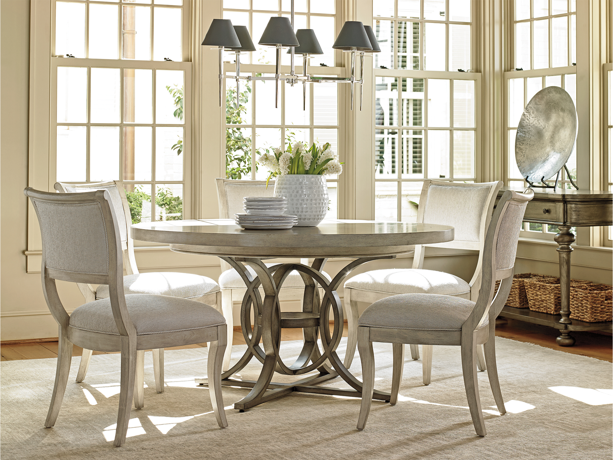 Lexington Oyster Bay — refined coastal dining room featuring a round gray-washed table with a decorative interlocking ring pedestal base, paired with elegant saber-leg dining chairs.