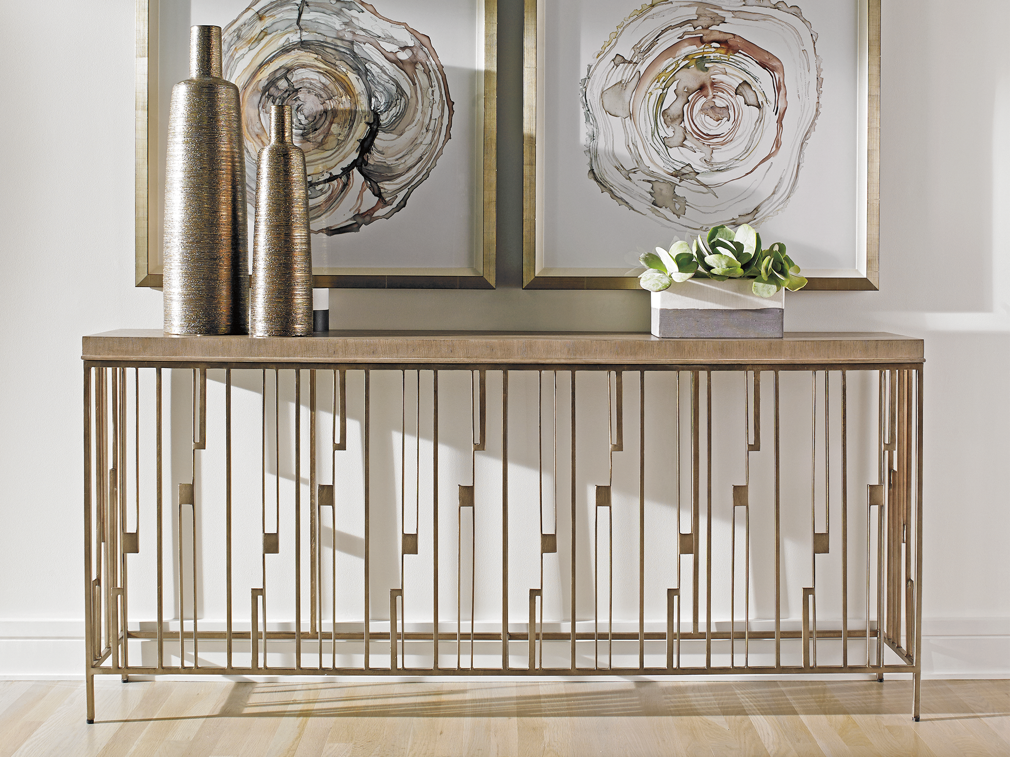 Lexington Shadow Play — Contemporary console table featuring a wood top and a geometric, linear metal base in a burnished gold finish. Anchored by organic wood-slice wall art and textured metallic vases for a sophisticated, modern entryway look.