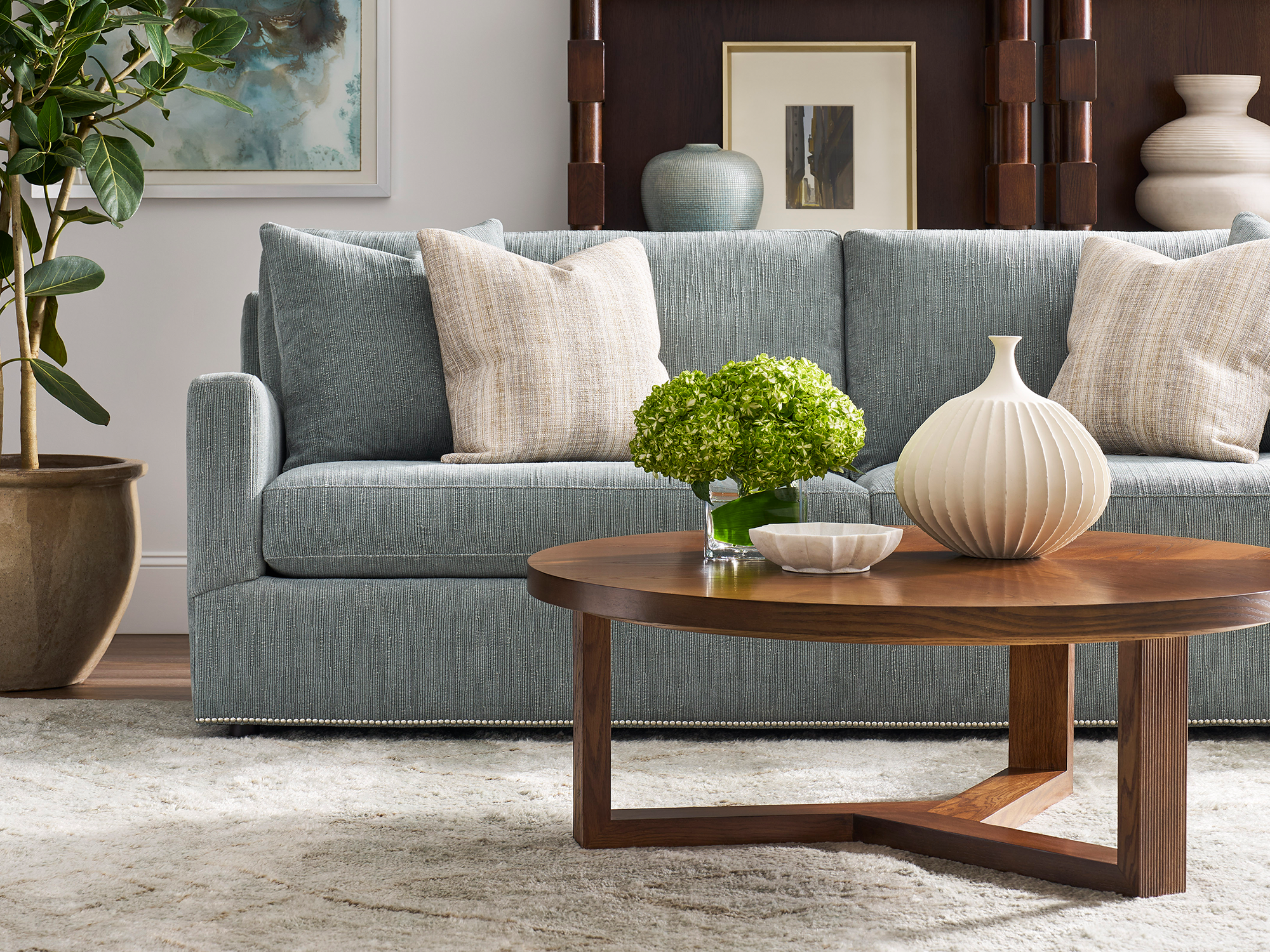 Sherrill 7 Series — modern transitional living room featuring a textured blue track-arm sofa with a decorative nailhead trim base, paired with a round walnut-finished wood cocktail table and neutral-toned accent pillows.