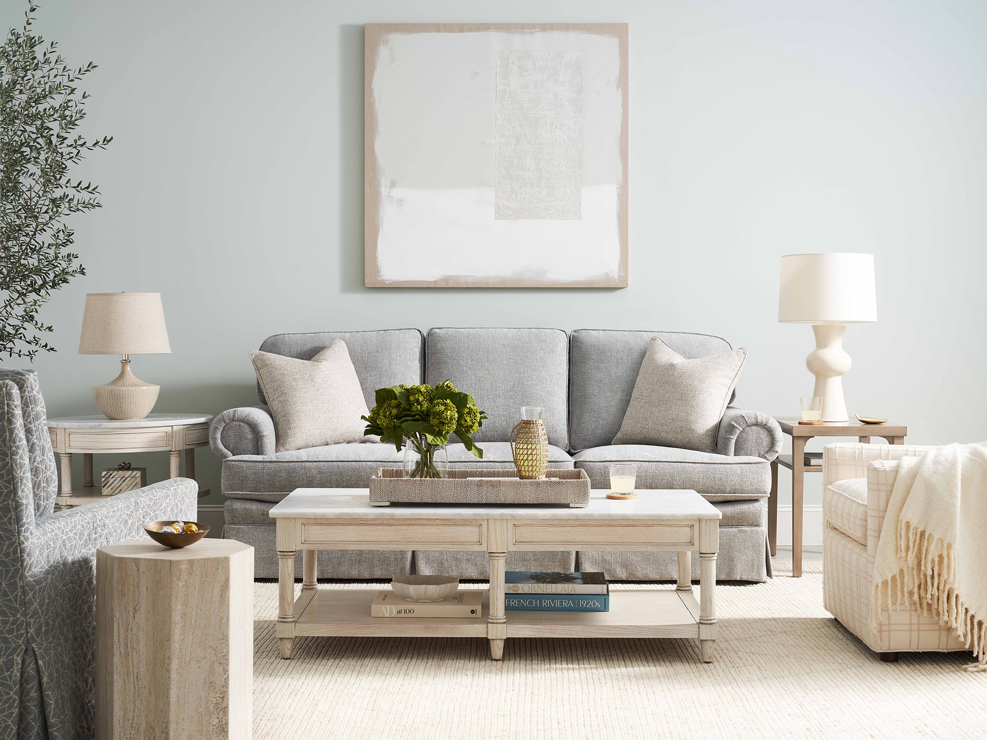 Sherrill 9800 Series — transitional living room featuring a light gray upholstered sofa with rolled arms and a dressmaker skirt, paired with a white marble-top cocktail table and matching end tables in a soft, airy neutral palette.
