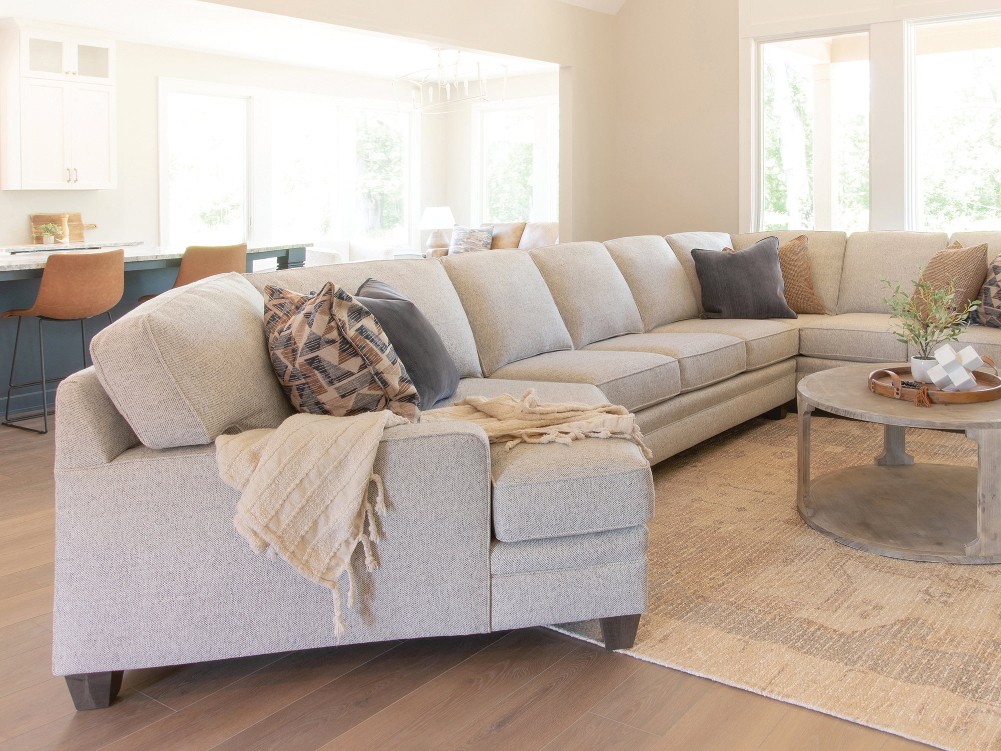Smith Brothers of Berne — spacious, sun-drenched living room featuring a large curved sectional sofa to maximize seating in an open-concept layout.