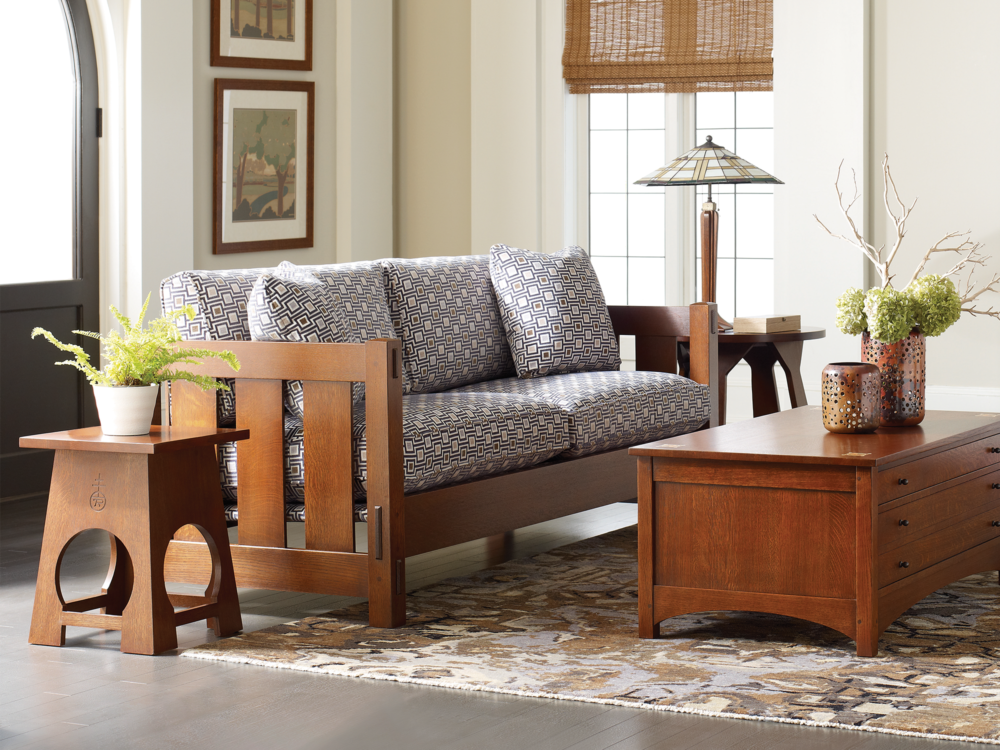 Stickley — classic Mission-style living room featuring a solid oak settle with spindle sides and geometric patterned cushions, paired with a matching oak cocktail trunk and a Roycroft-inspired side table with circular cutouts.